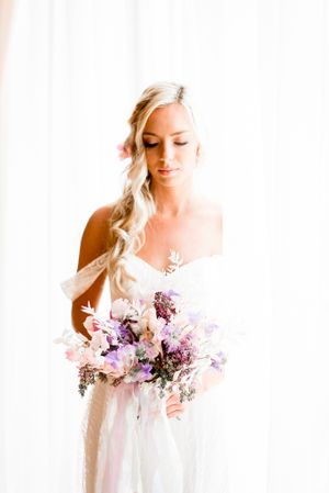 blonde bride with braided hair looking at her colorful purple and pink spring wedding bouquet