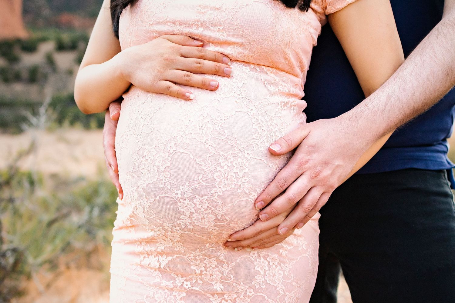 Close up of pregnant bump, pink dress, woman and mans hands on the bump