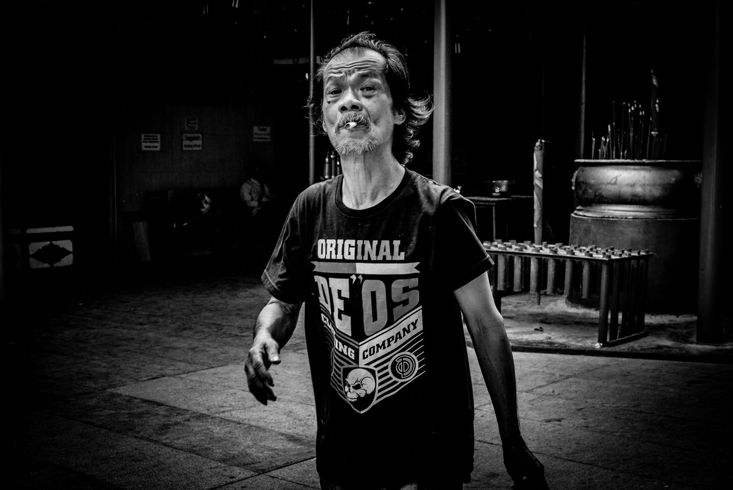 Black and white photo fo man smoking and walking at buddhist temple in Gloodok district of Jakarta Indonesia