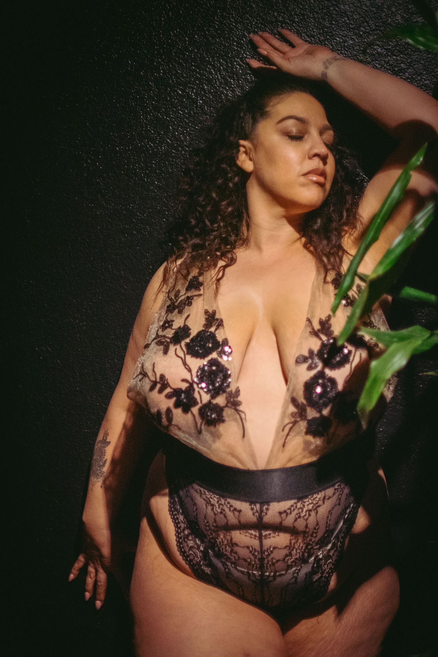 Plus size woman in lingerie posing in lingerie againt wall with plant