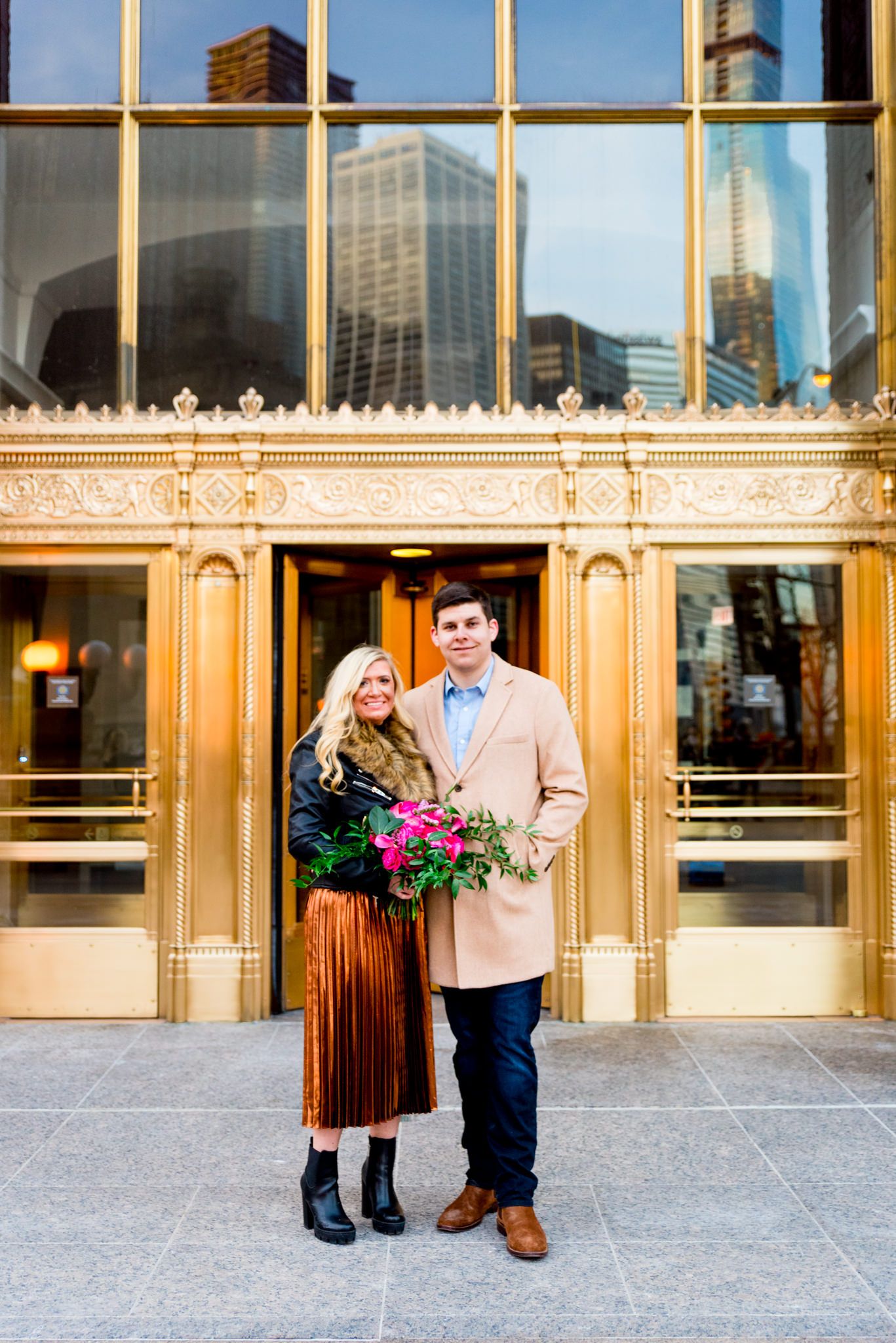 blonde woman and her fiance walk in front of gold doors at Wrigley Building engagement pictures