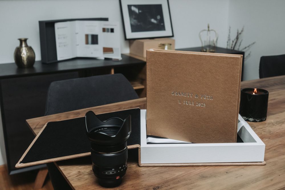 Brown linen photo album in white presentation box with camera equipment.