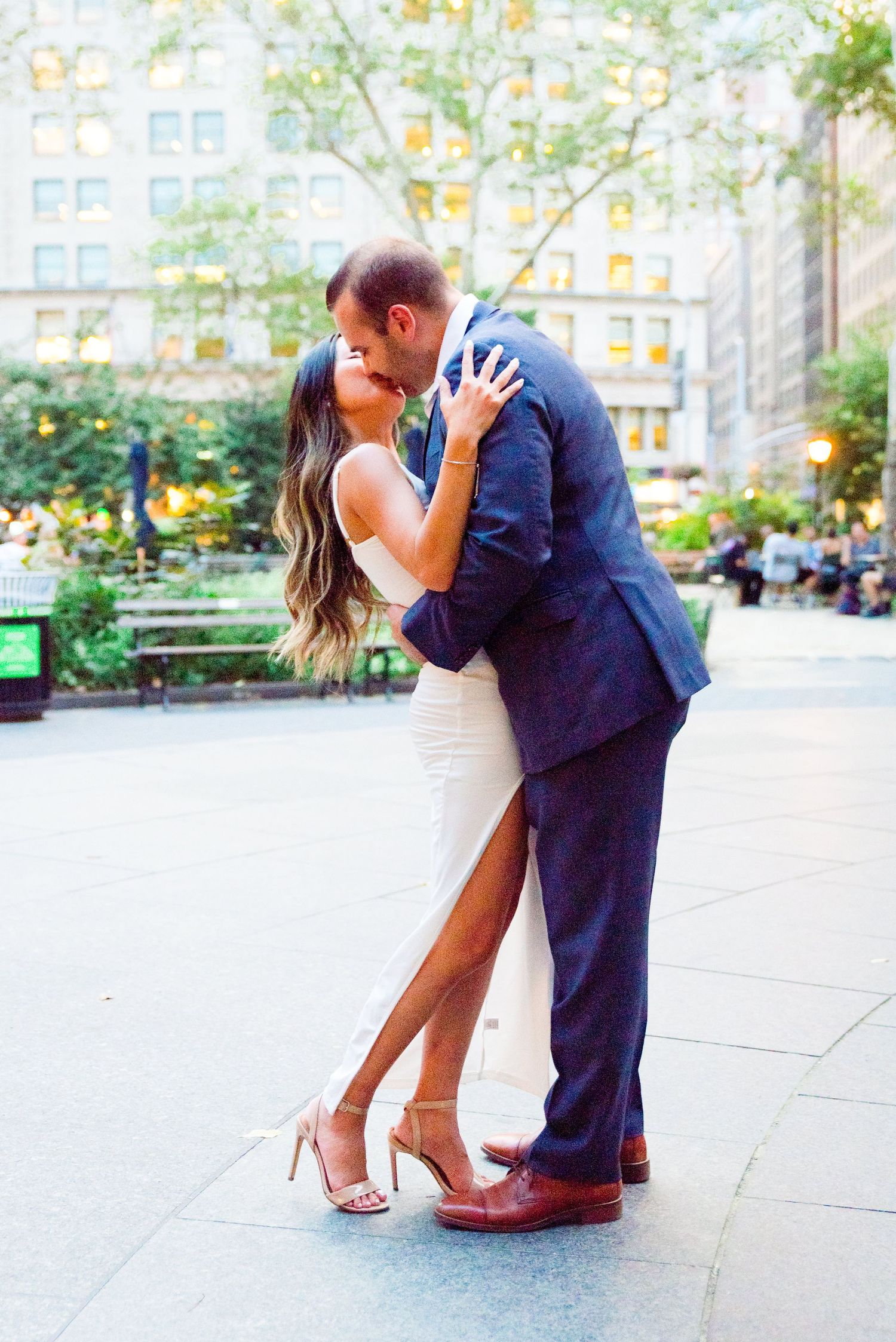 fiances in white and navy kissing each other in front of building in Madison Square Park at sunset