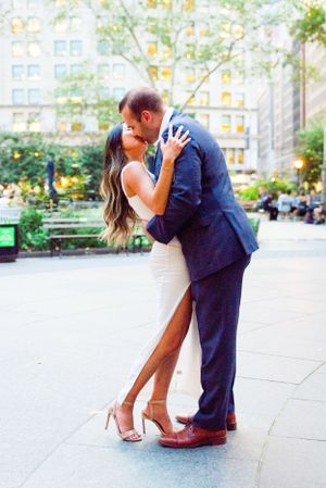 fiances in white and navy kissing each other in front of building in Madison Square Park at sunset