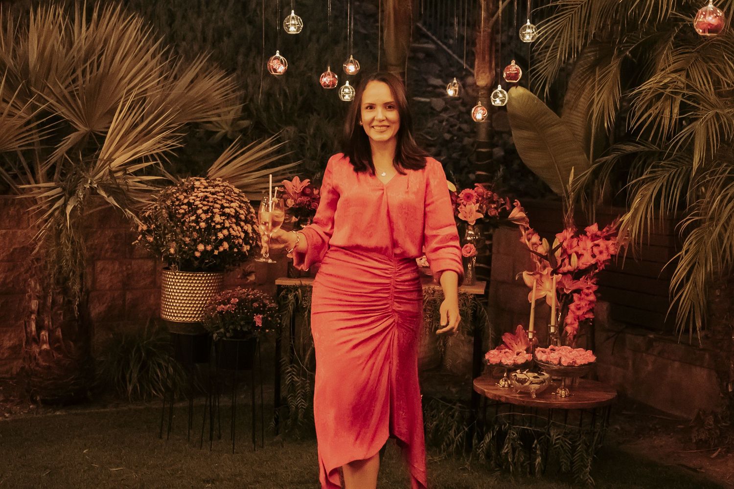 Person in coral dress posing against tropical backdrop with hanging lights.