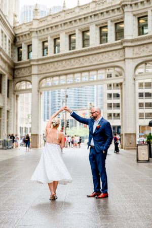 couple in navy suit and glittery dress with red bouquet walking under Wrigley building at Chicago Elopement