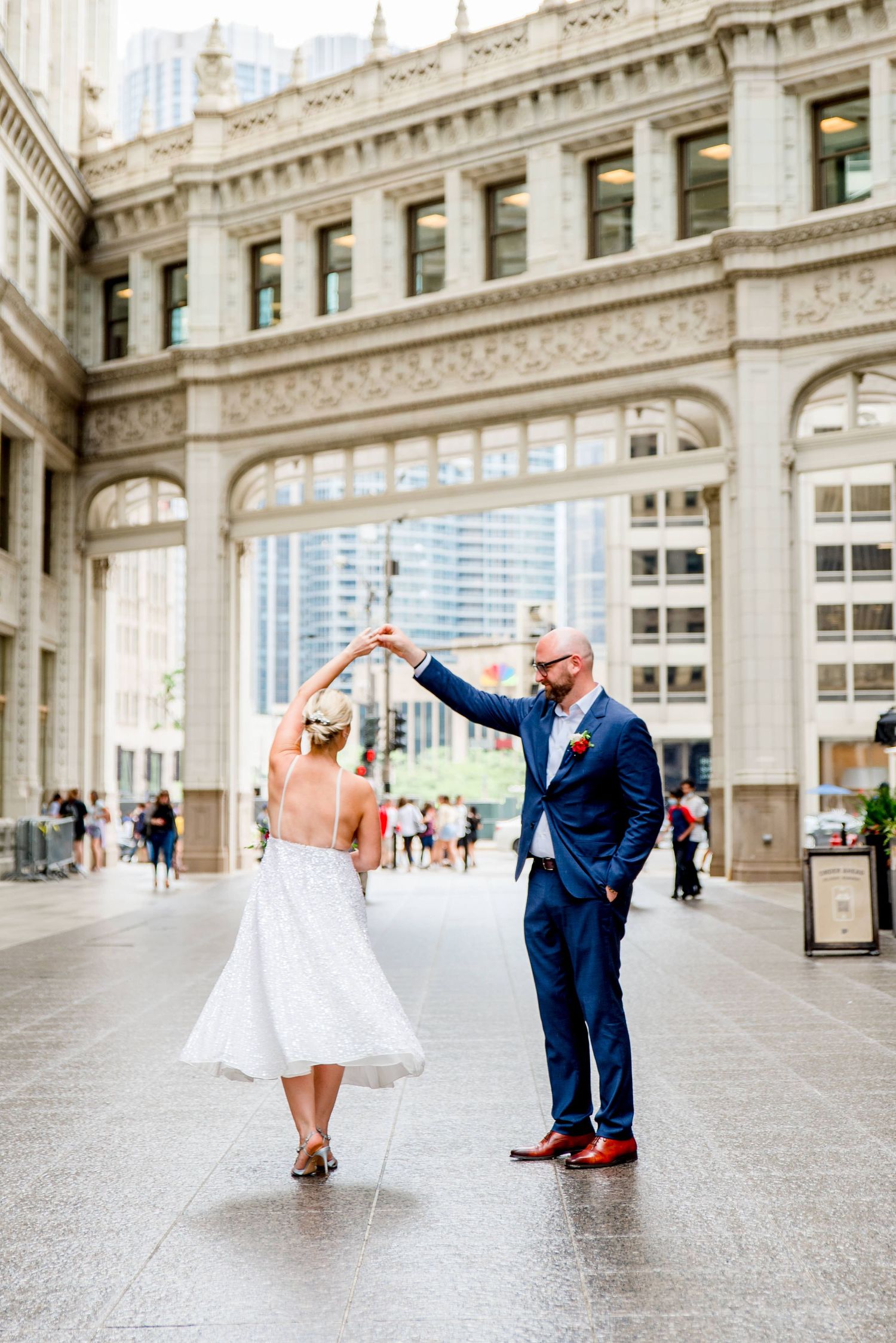 couple in navy suit and glittery dress with red bouquet walking under Wrigley building at Chicago Elopement