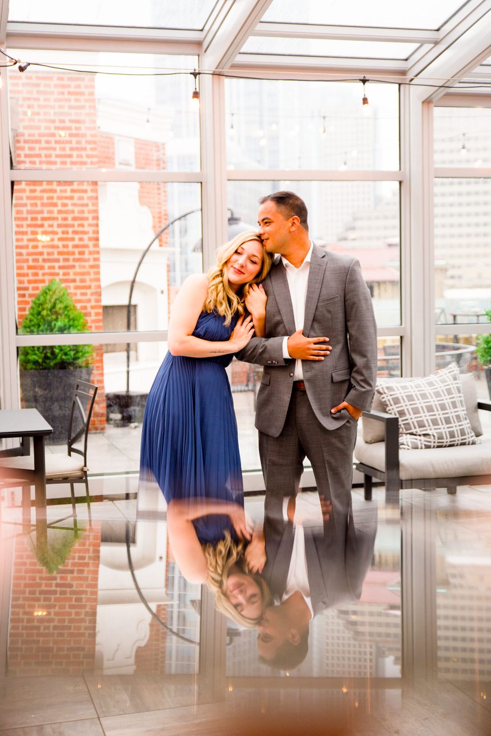 young woman in blue dress hugs fiance's arm and leans on his shoulder at Lytle Park Hotel Vista rooftop