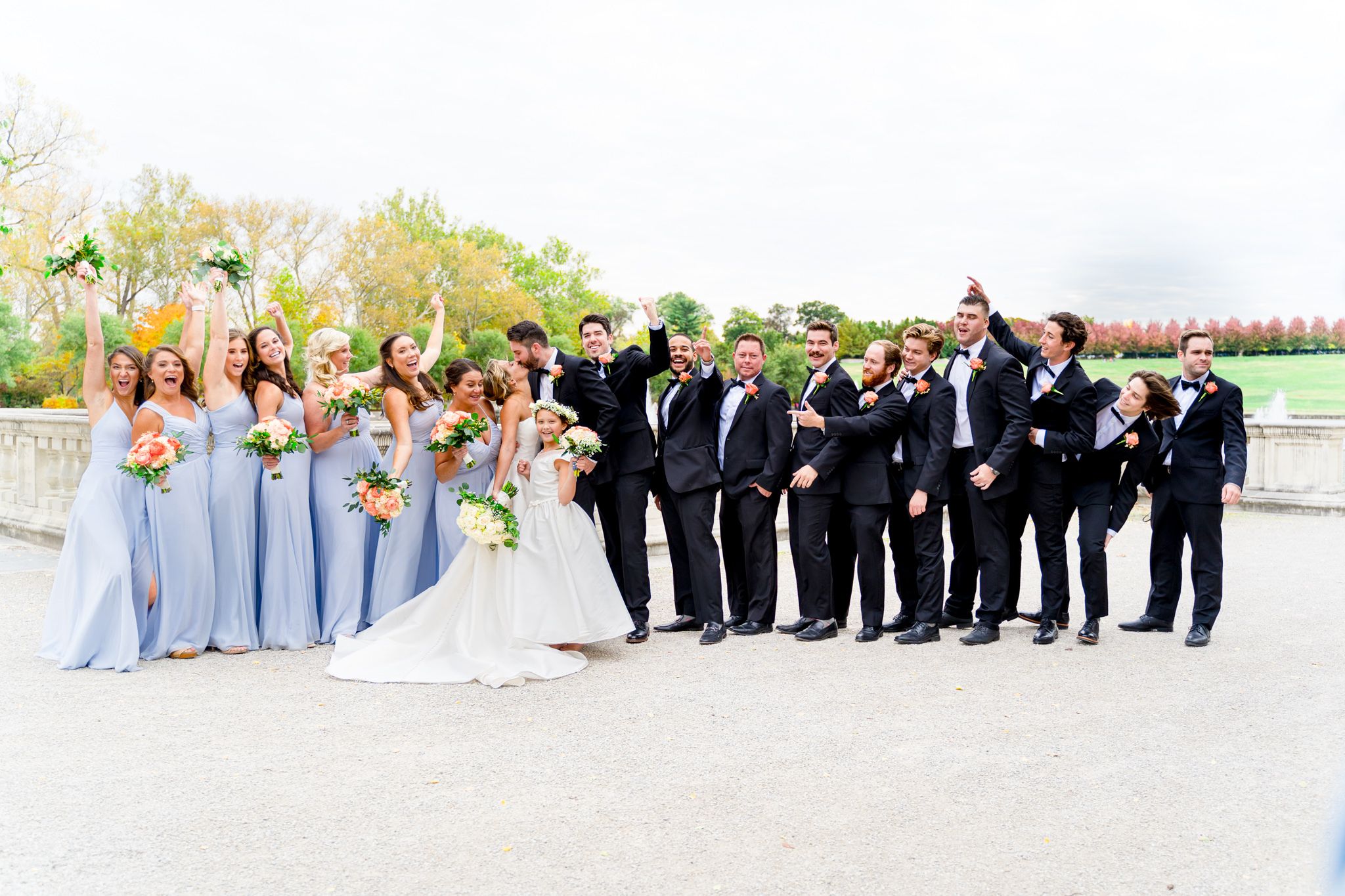 large wedding party in black suits and light blue dresses surround bride and groom at Forest Park in St. Louis