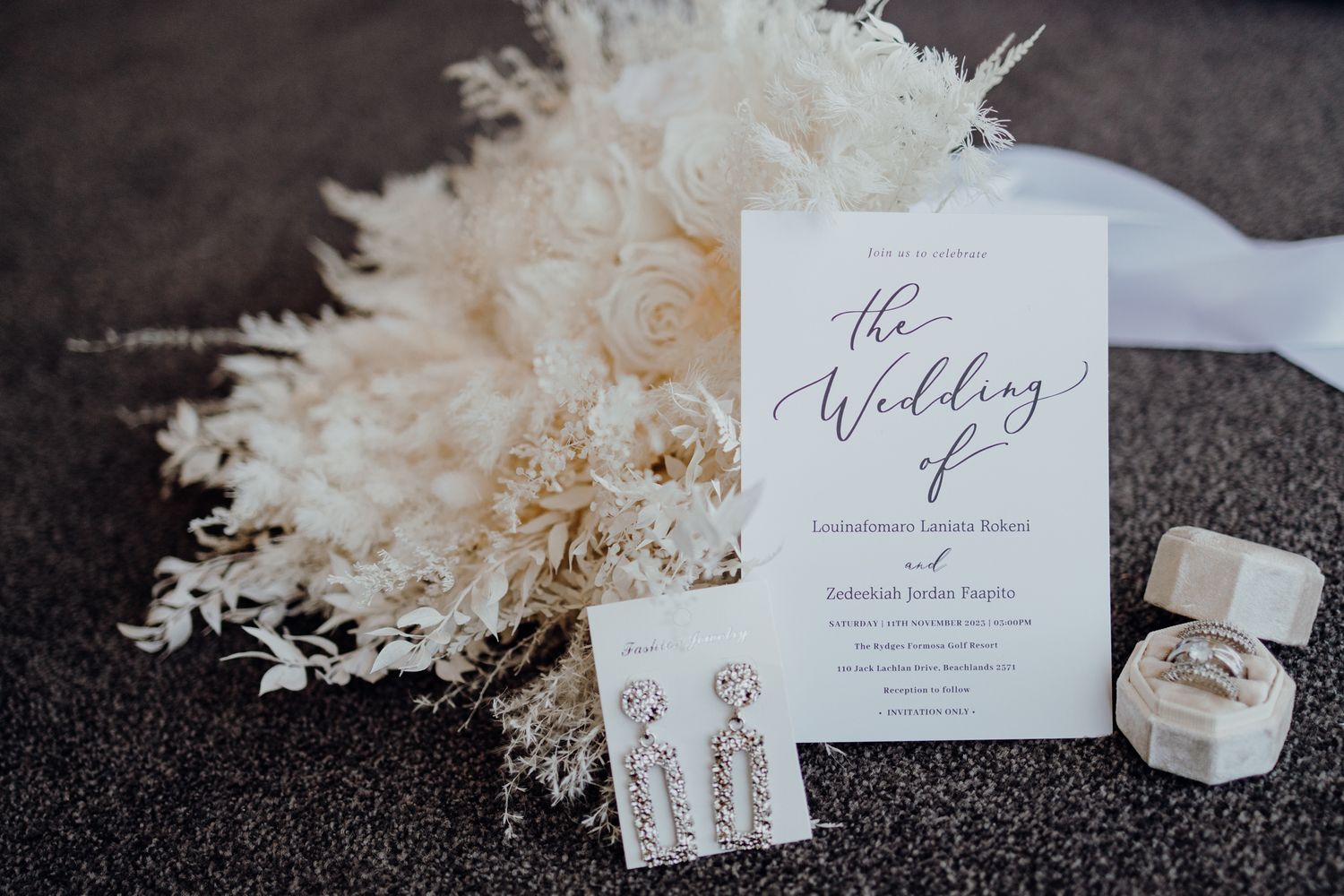 Wedding invitation with elegant calligraphy displayed with dried flowers and a ring box.