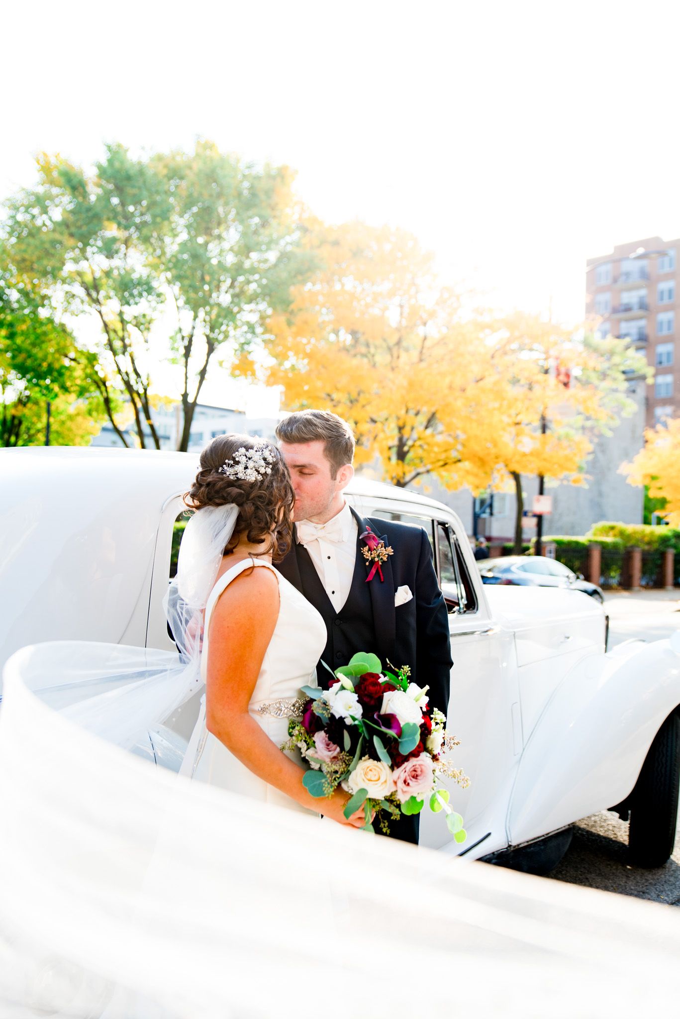 colorful photography of bride and groom kissing in front of antique white car
