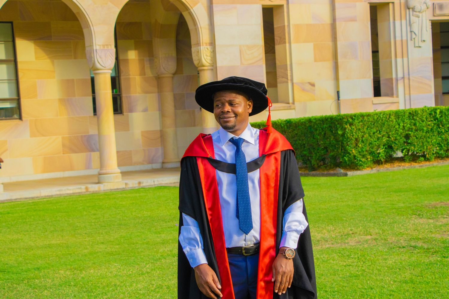 Graduate in academic regalia standing on university campus lawn.