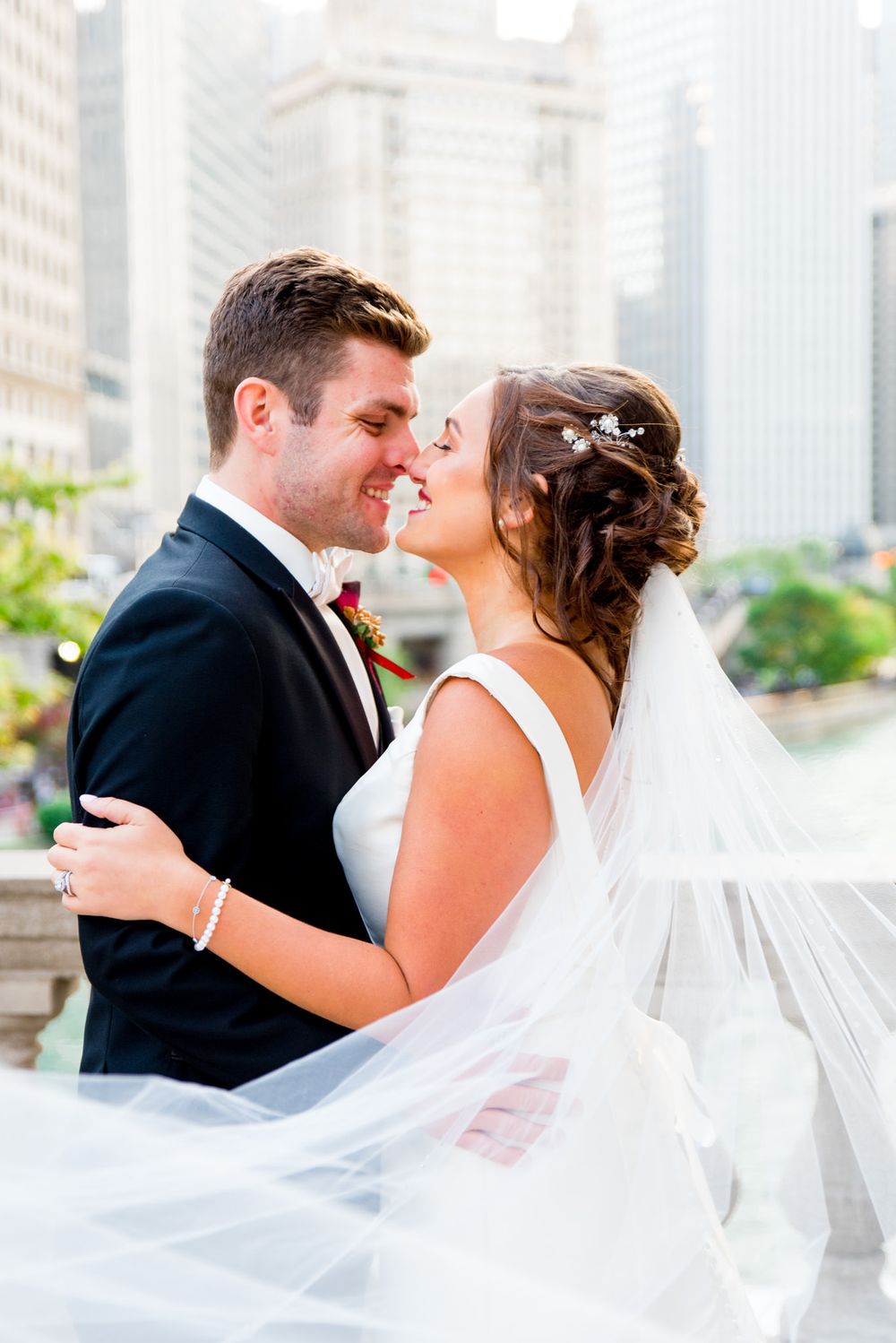 bride wearing a jeweled barette caresses her groom on a bridge in downtown chicago