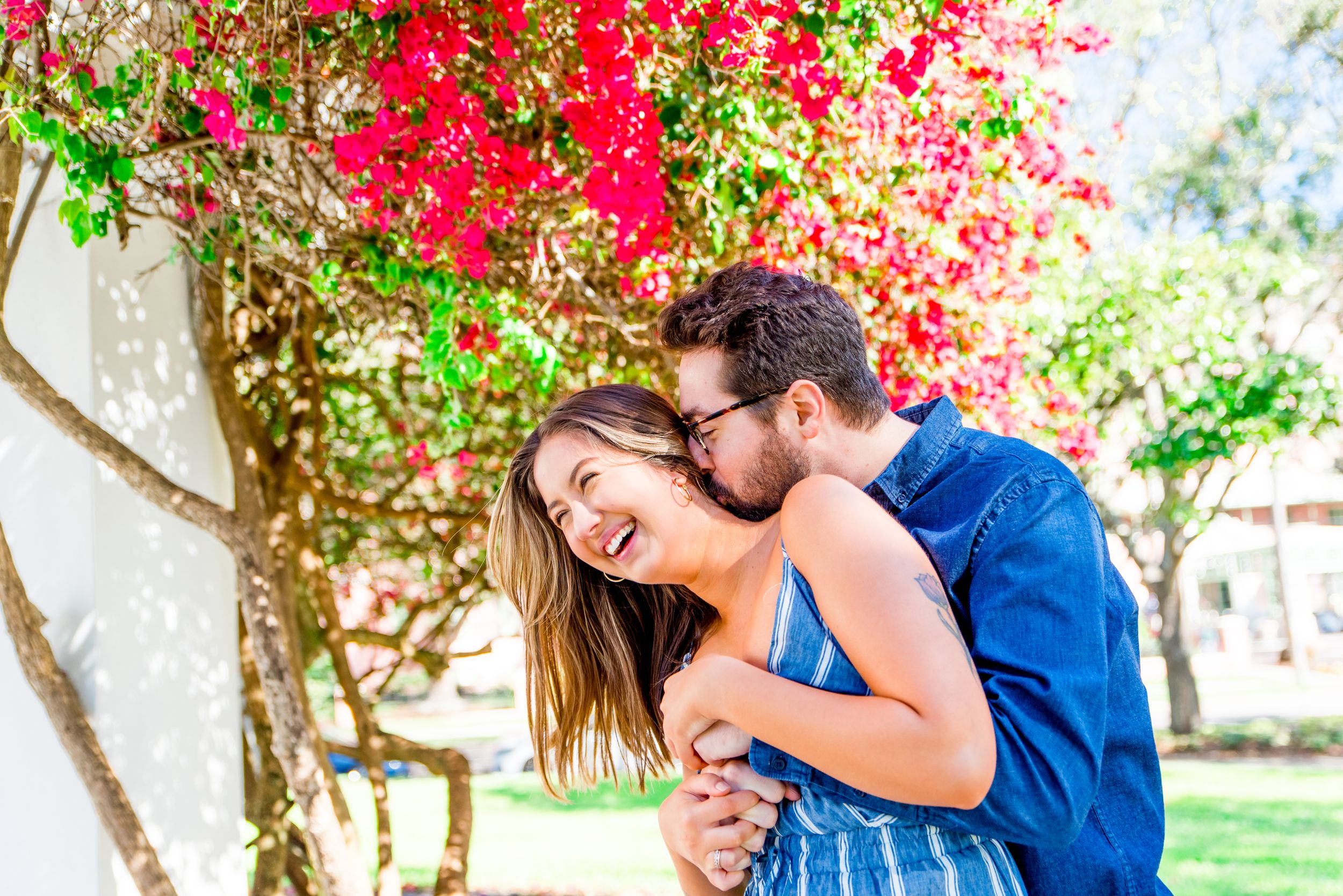 young man kissing woman's neck under pink flower tree at Vinoy Park, St Pete engagement photos