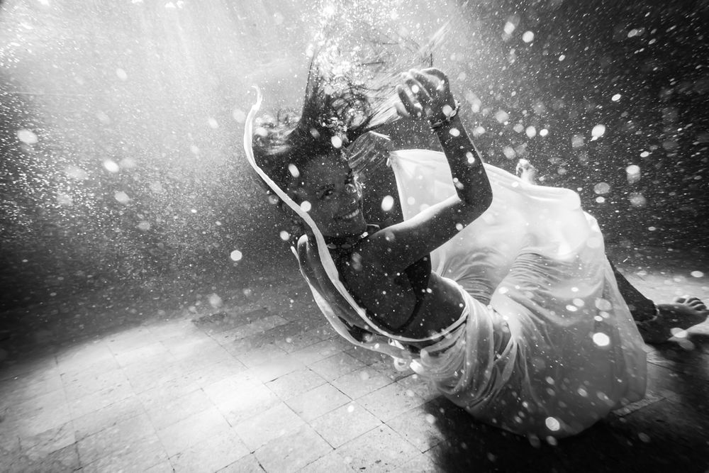 A woman smiling underwater wearing a white dress