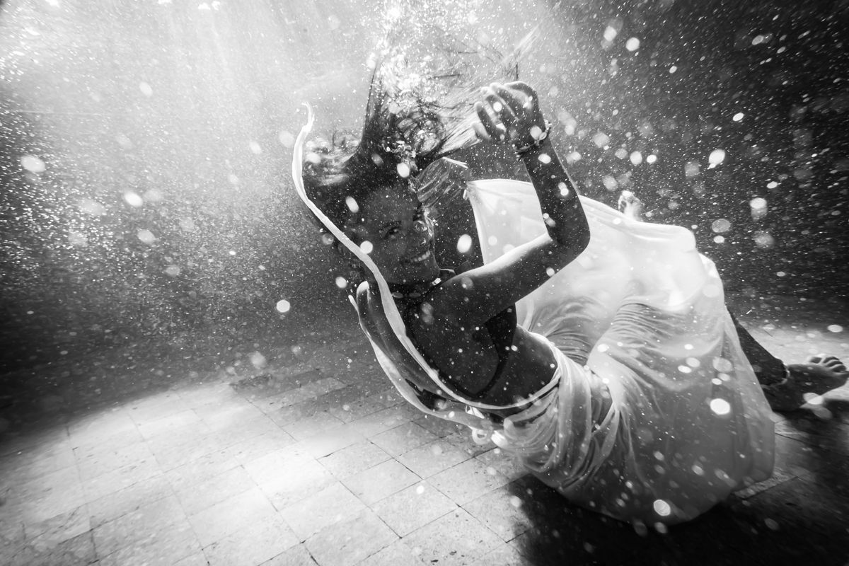 A woman smiling underwater wearing a white dress