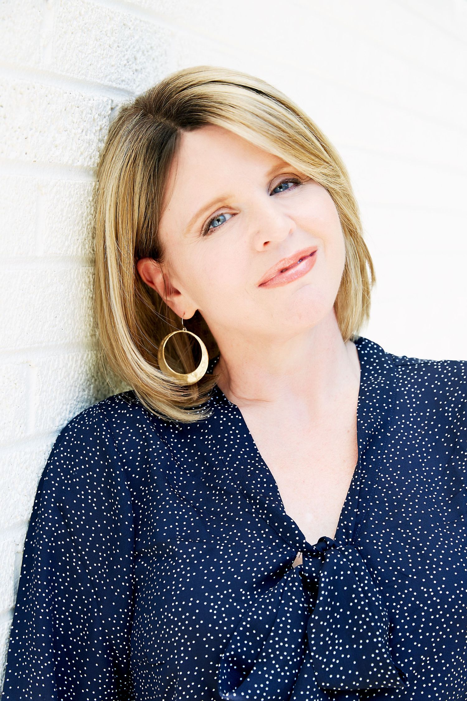 Professional headshot featuring polka dot navy blouse against white background.