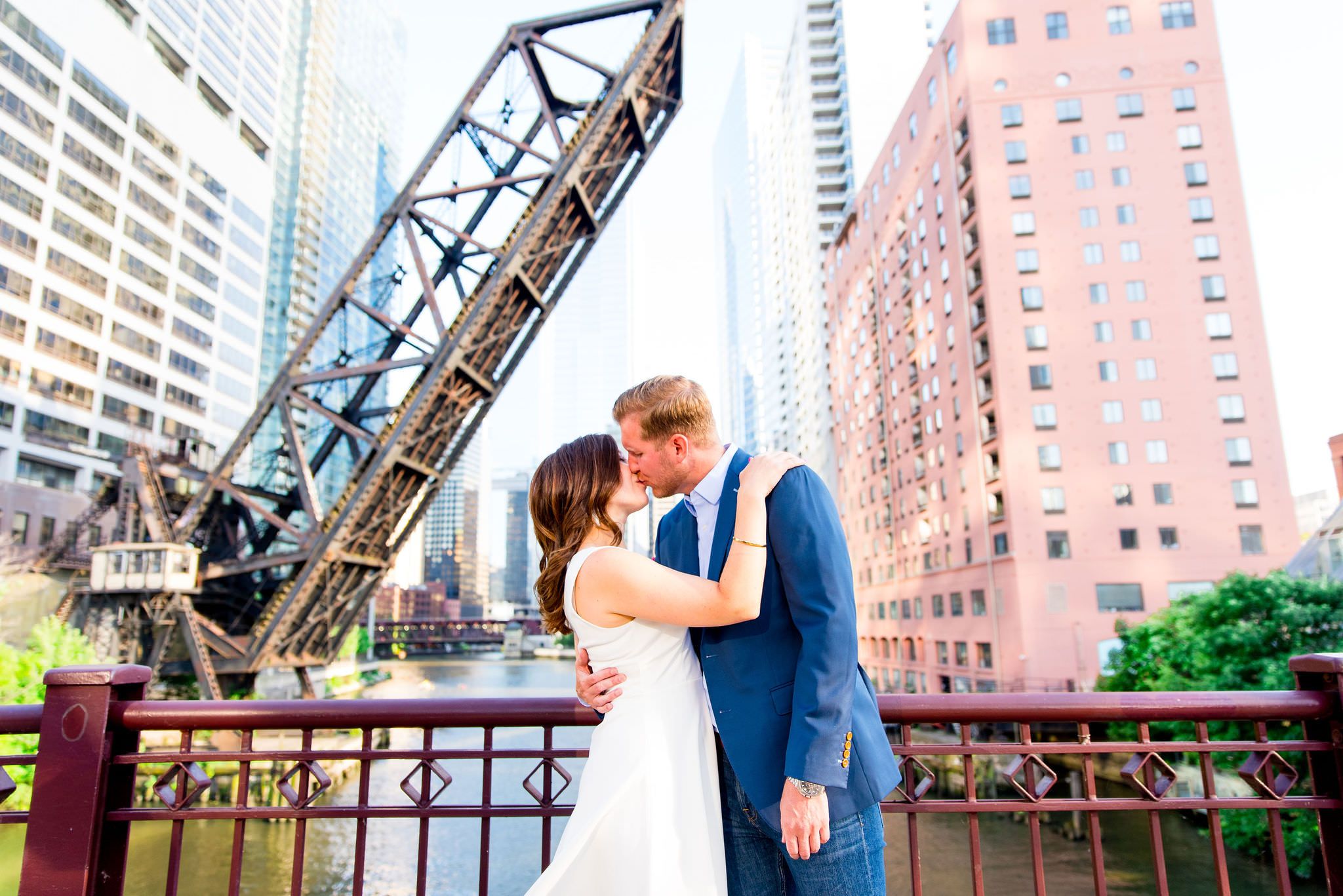 man in navy suit and woman in white dress kissing in front of Chicago River for sunset engagement pictures in Chicago