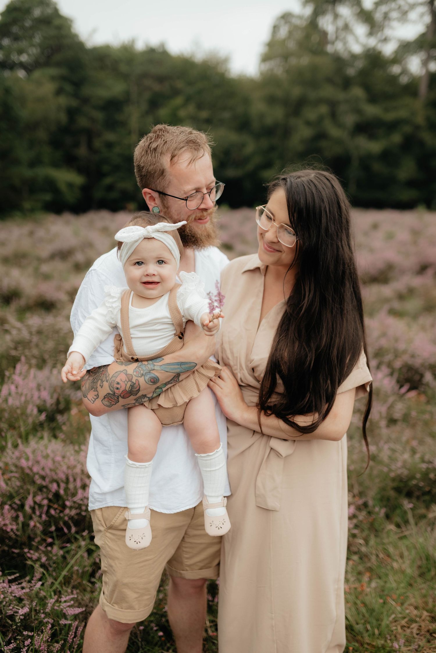 A family stands together in a field of blooming purple heather during a warm summer evening.