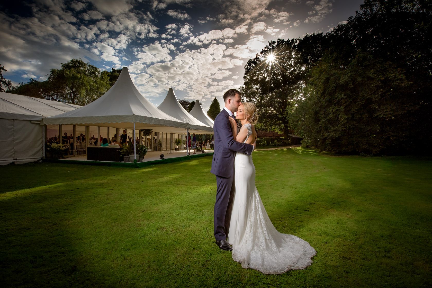 Groom holds his bride in her white wedding dress on a Summer evening outside their wedding marquee in a Cheshire garden