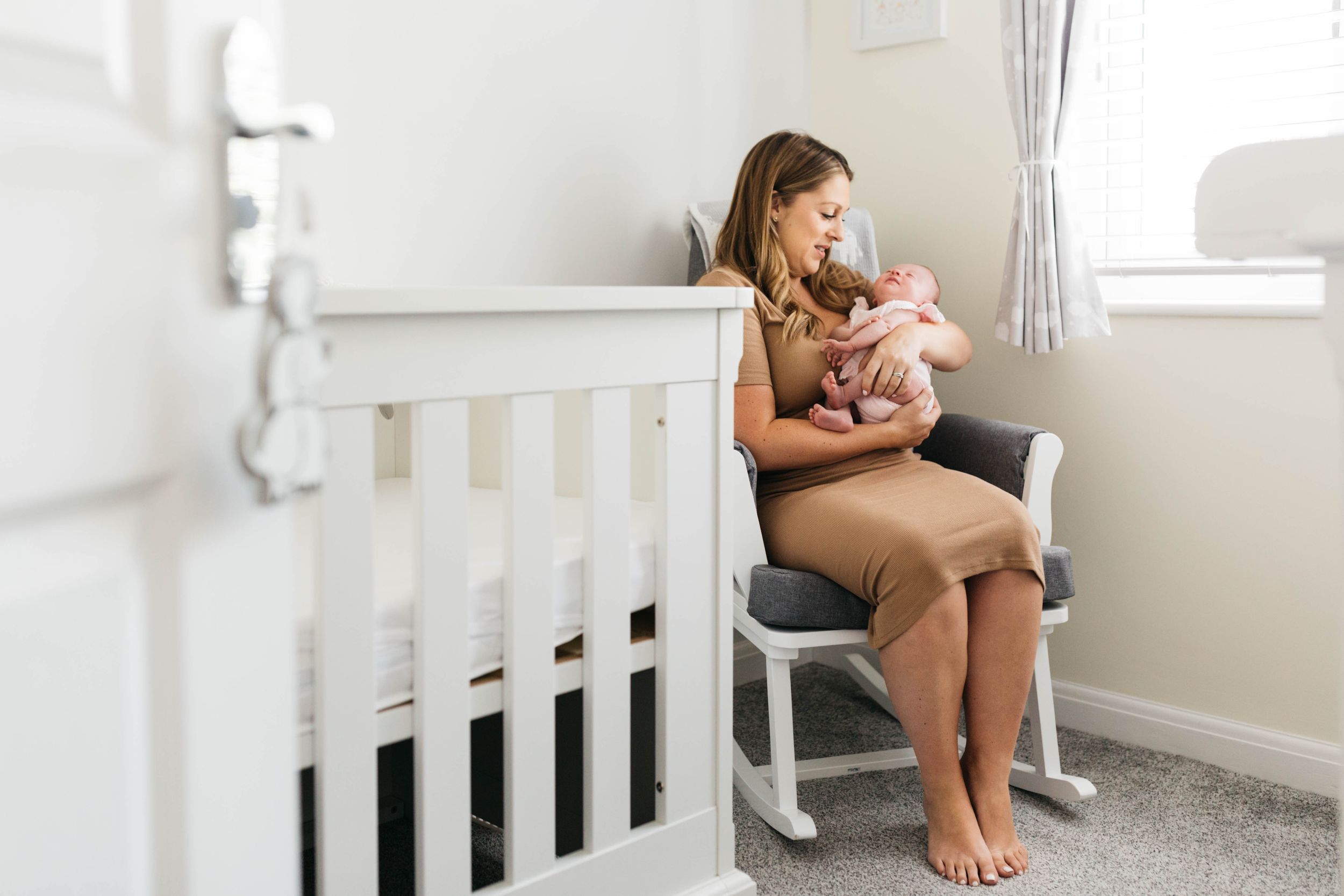 mum sitting in rocking in baby room holding newborn daughter
