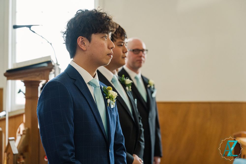 Groomsmen in navy suits with boutonnieres stand at attention during church ceremony.