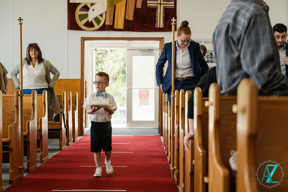 Young ring bearer in formal attire walks down red-carpeted church aisle.