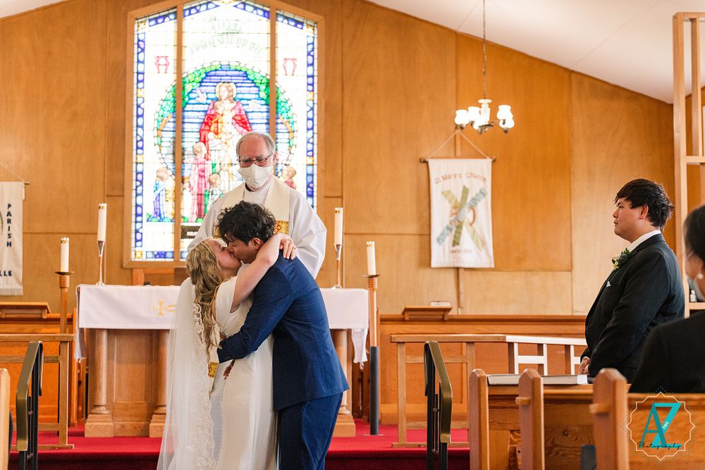 Intimate wedding ceremony moment in church with stained glass window backdrop.