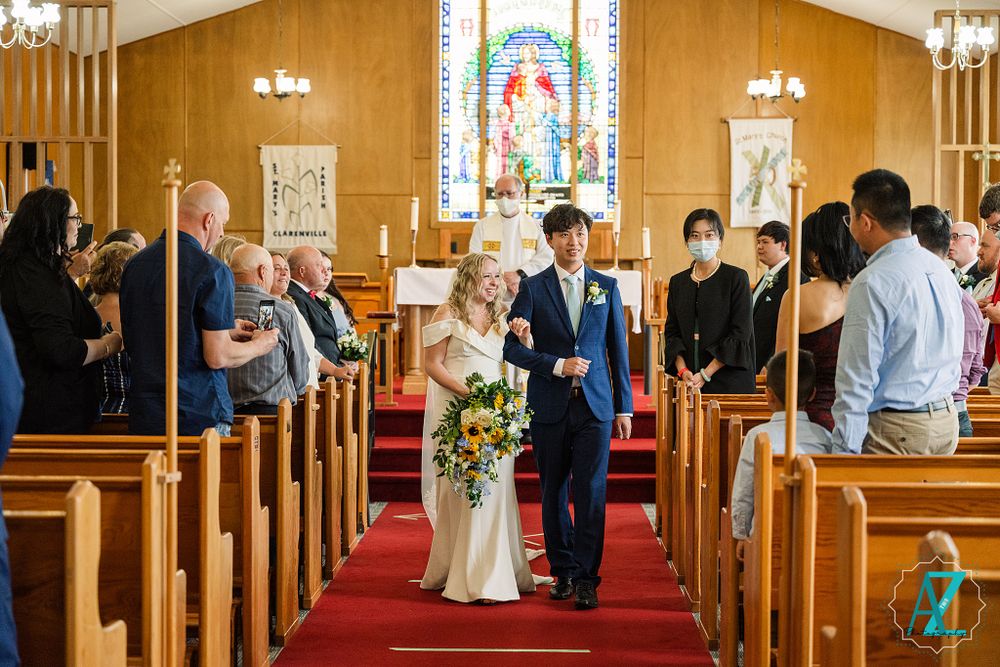 Newlyweds exit church ceremony down red-carpeted aisle as guests look on.