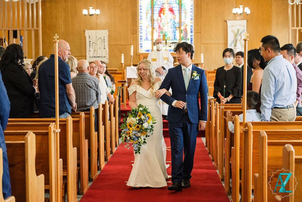 Wedding recessional in traditional church with wooden pews and red carpet aisle.