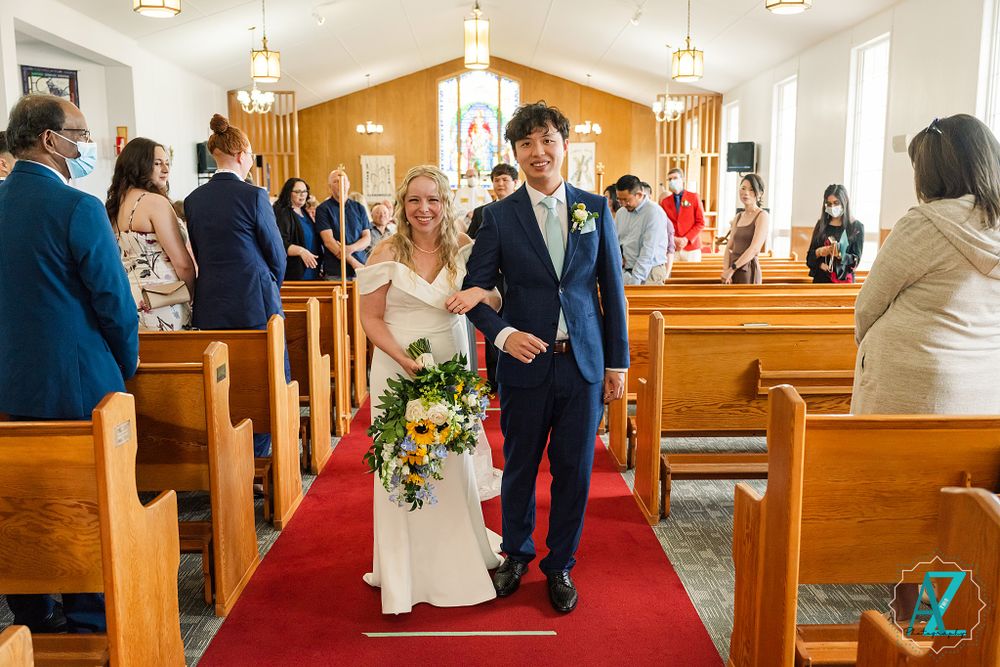 Wedding couple exits down the red-carpeted church aisle while guests look on from wooden pews.