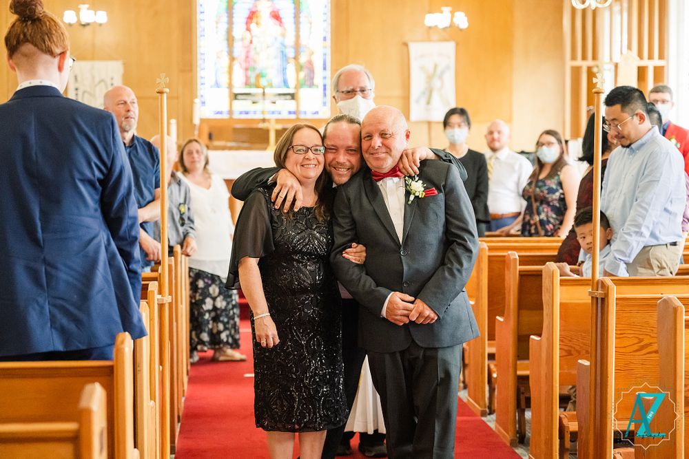 Wedding guests smile and celebrate inside a church with stained glass windows and wooden pews.