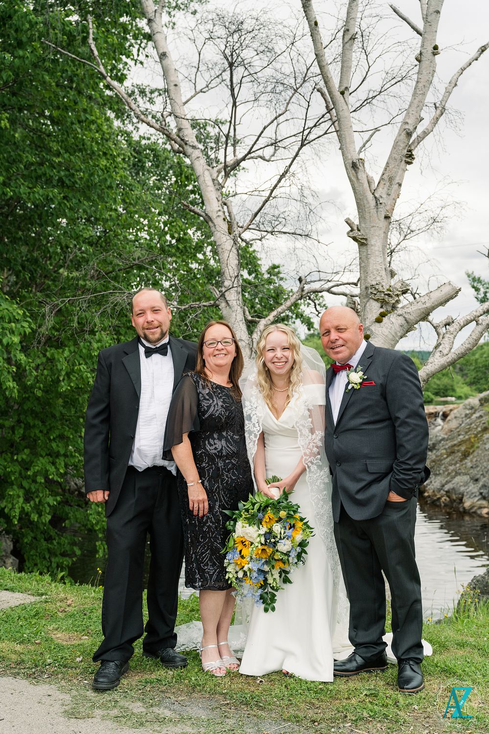 Wedding group photo with formal attire and sunflower bouquet against scenic outdoor backdrop.