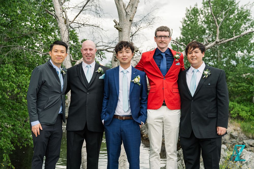 Groomsmen in formal attire stand together against natural backdrop with white birch trees.