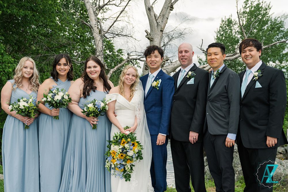 Wedding party with bridesmaids in light blue dresses and groomsmen in dark suits pose by birch trees.
