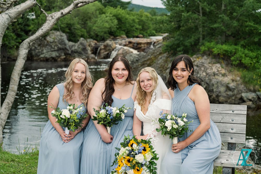 Bridal party with sunflower bouquets poses by waterfront in light blue bridesmaid dresses.