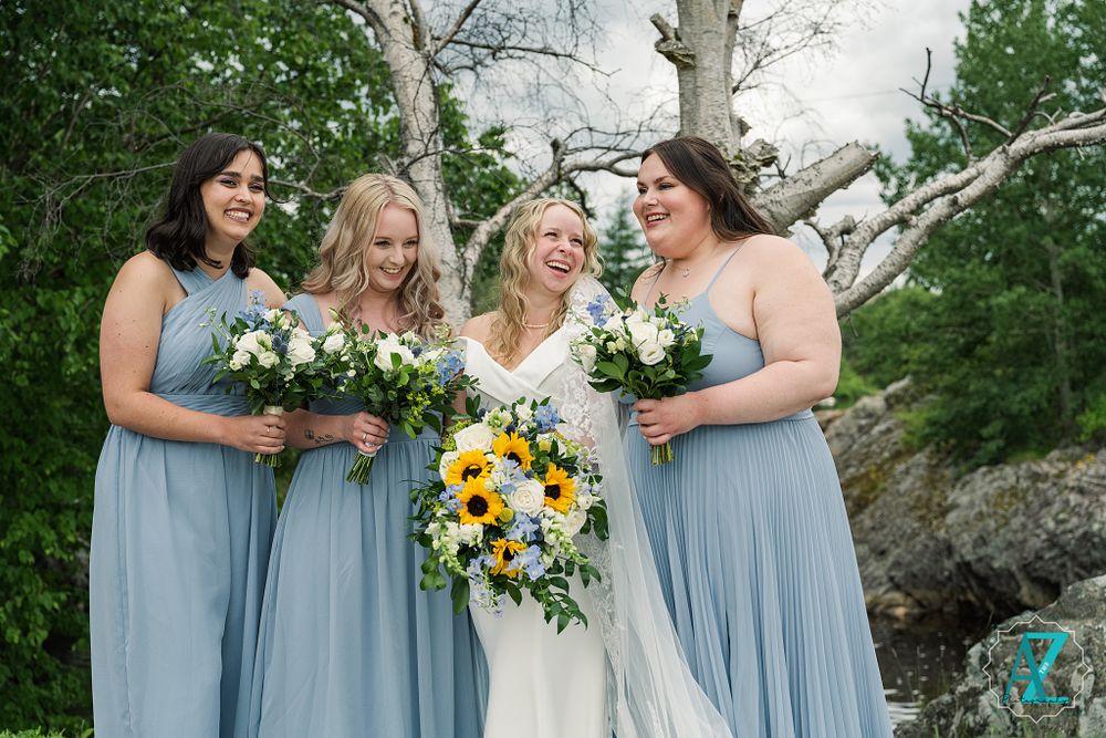 Bridal party smiling with bouquets of white and yellow flowers wearing powder blue dresses in an outdoor setting.