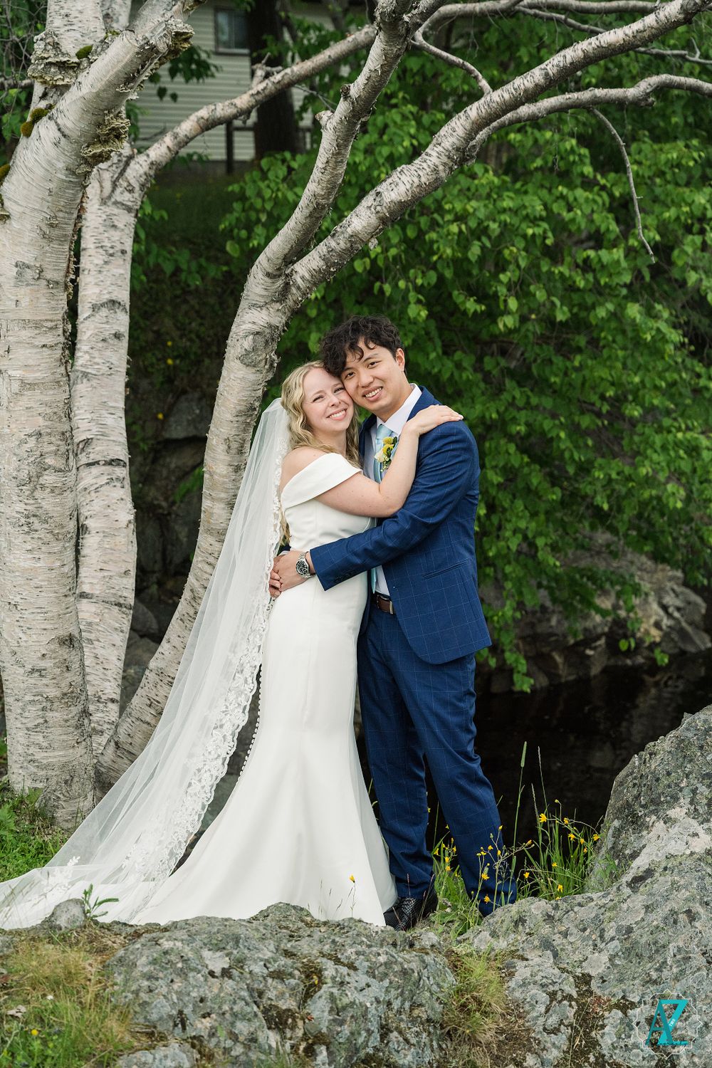 Wedding couple embracing by birch trees with long veil and classic navy suit.