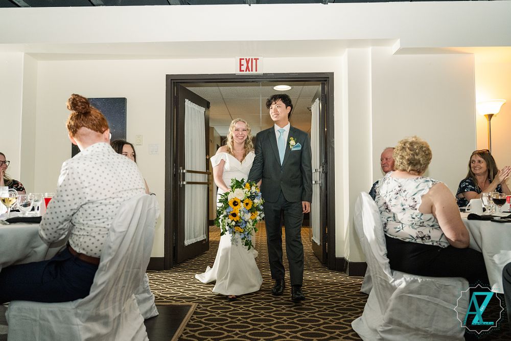 Wedding couple makes their reception entrance while guests seated at tables look on.
