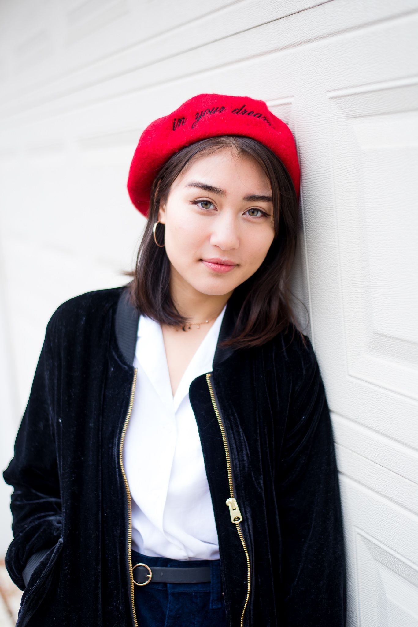 young woman with dark hair and red beret leaning against white garage