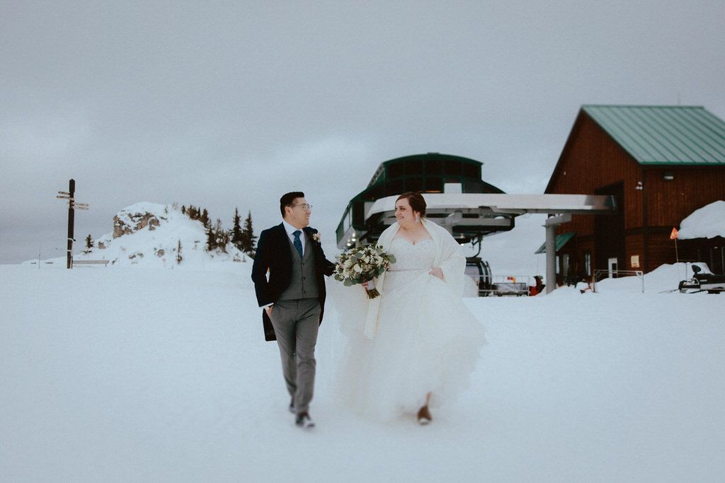 A winter wedding photoshoot in a snowy landscape with rustic cabins in the background.