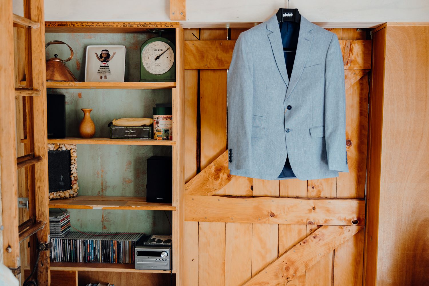 Light blue suit jacket hangs on wooden wall next to rustic shelving unit with decor items.