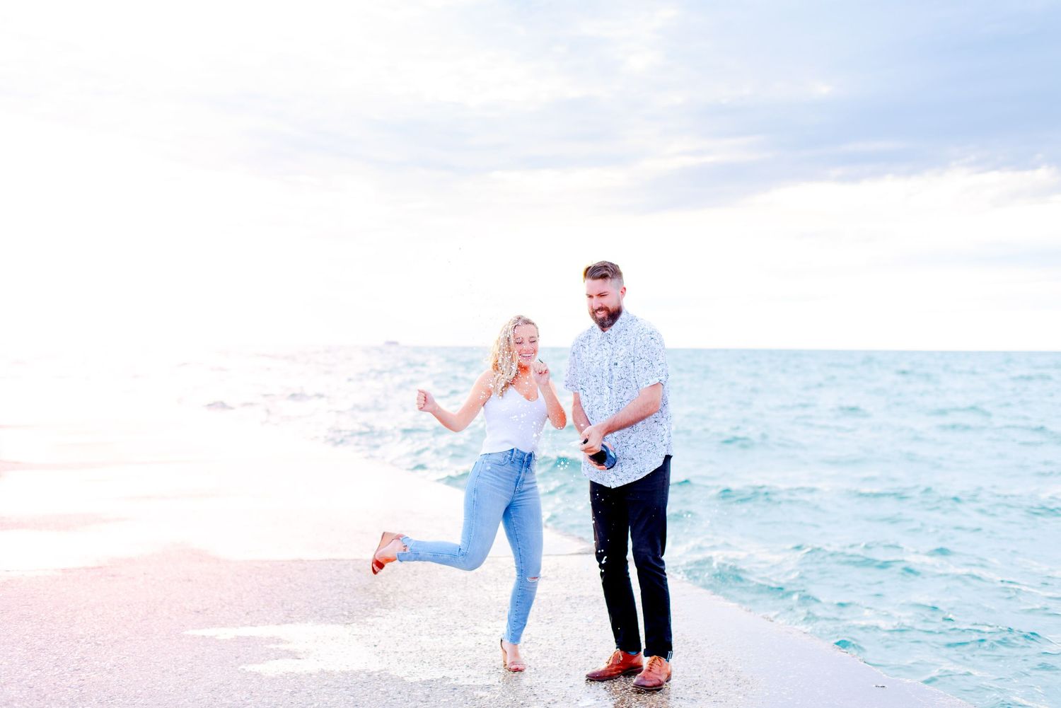 young engaged couple dances and pops champagne at Chicago North Avenue Beach pier during sunrise