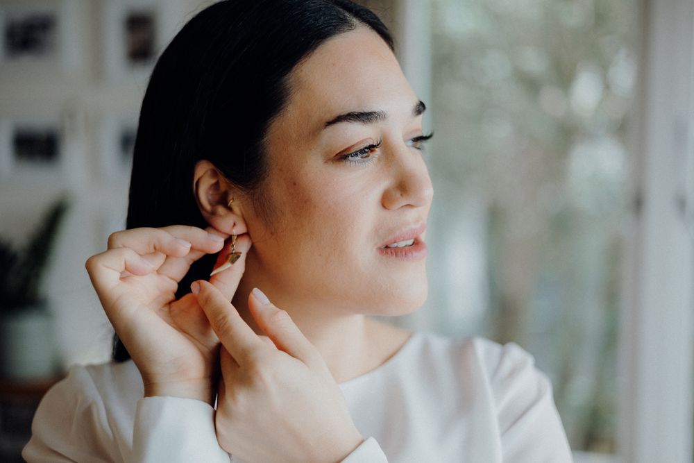 Close up shot of woman putting on earrings while getting ready near window.