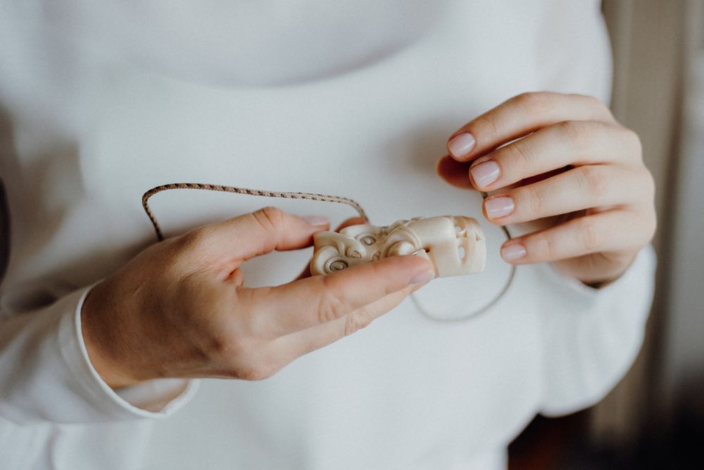 Close up of hands holding delicate jewelry against white clothing.