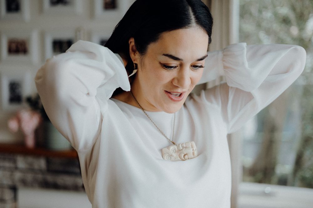 Woman in white sweater smiling with hands behind head in natural light.