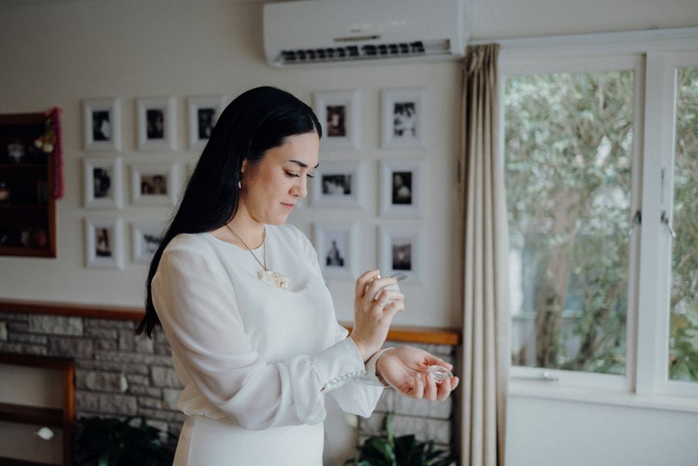 Woman in white dress admiring jewelry by window with photo gallery wall in background.