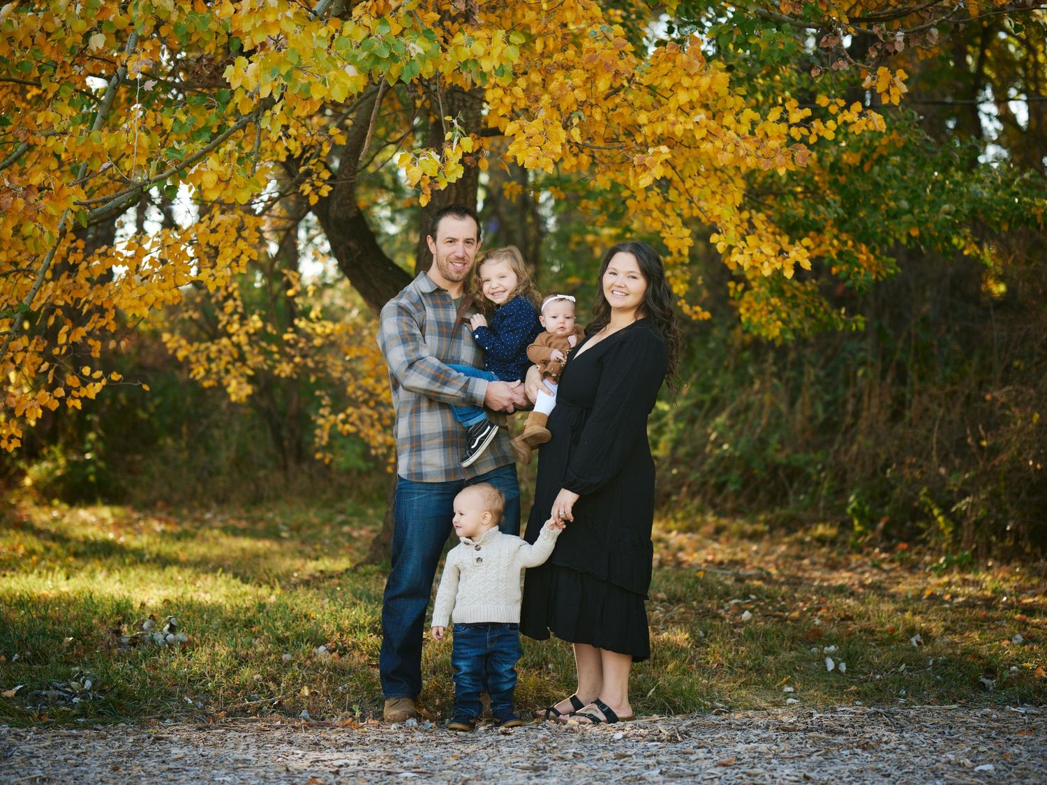 A family poses together under golden autumn foliage on a sunny fall day.