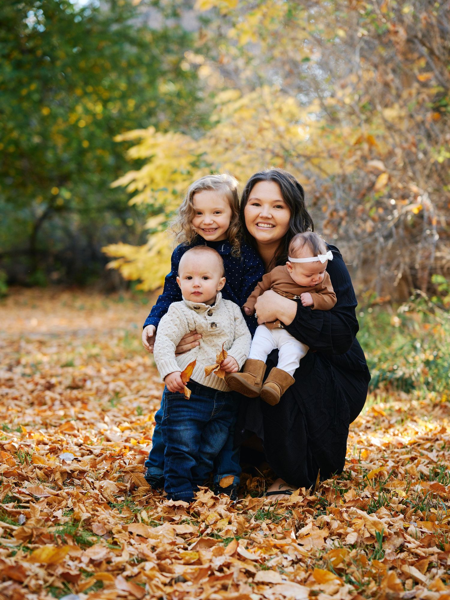 A group sits together on fallen leaves under golden autumn trees.