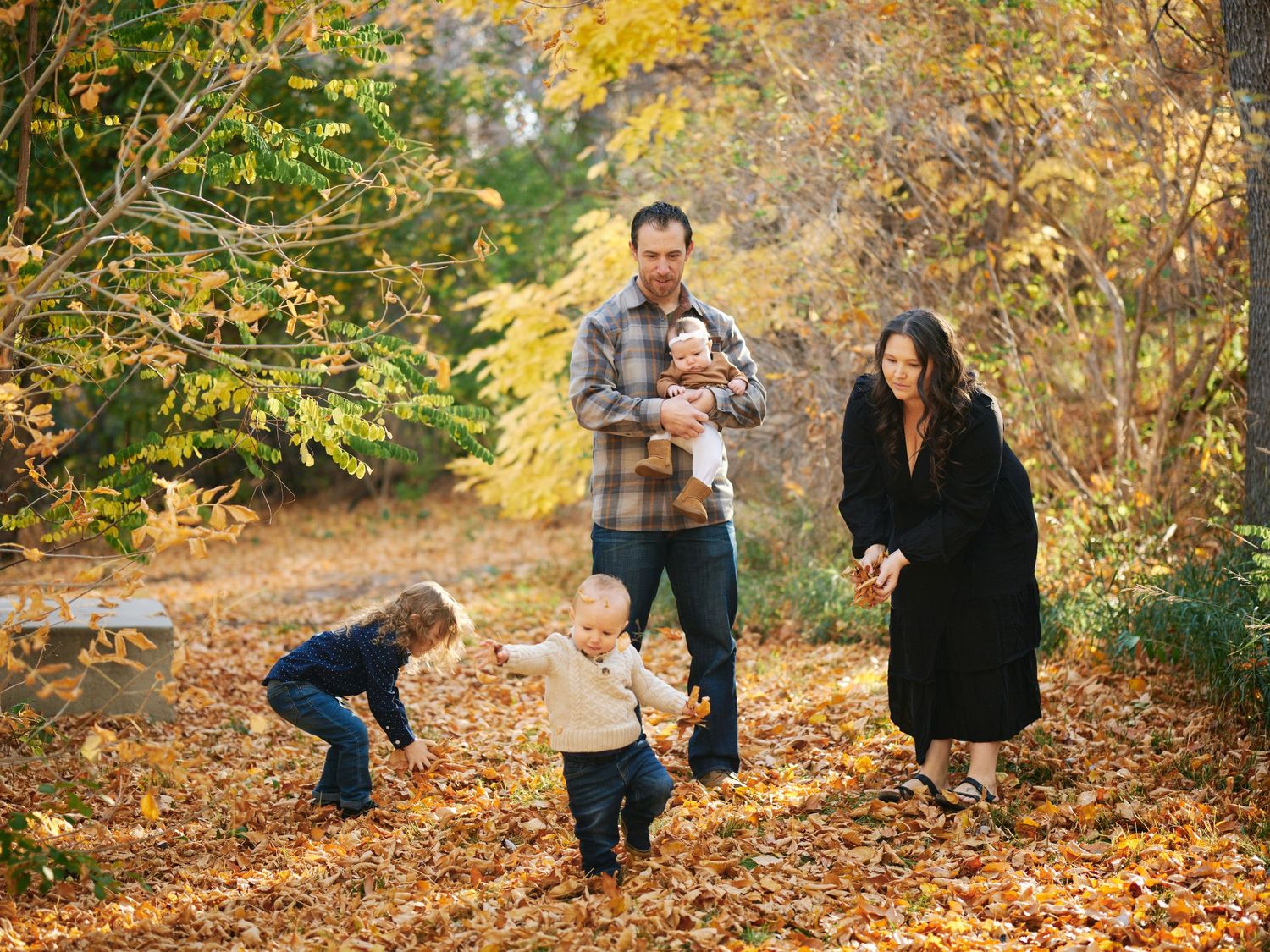 A family plays together in a park covered with fallen autumn leaves.